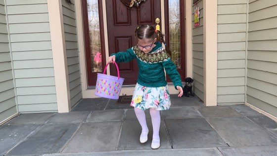 a little girl donning a hand knitted sweater and flower dresshops off the front steps of a house in search of Easter eggs