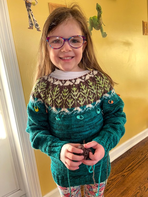 a little girl models a hand knitted sweater in progress
